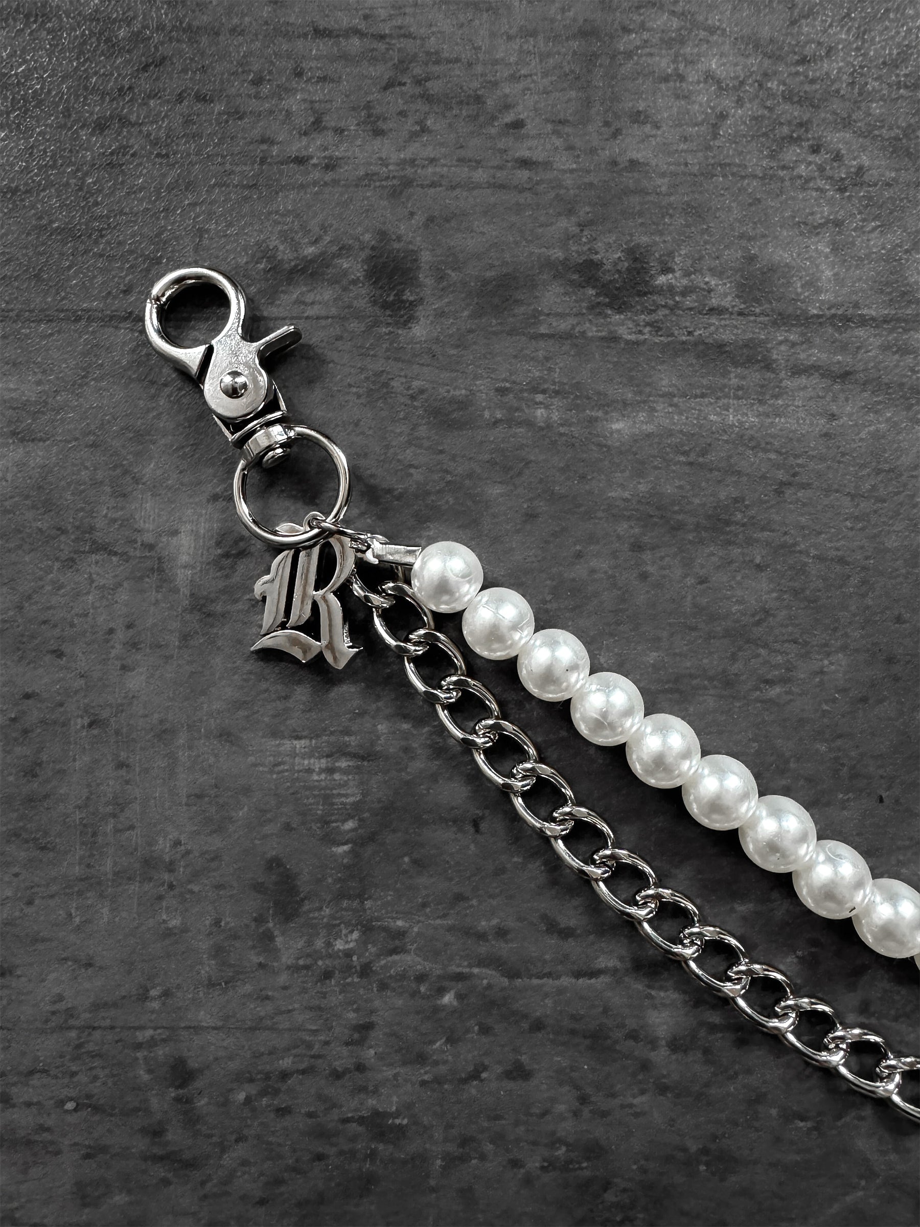 Pearl chain with silver clasp and 'R' charm on a dark textured background